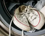 Weiße Turnschuhe mit roten Streifen liegen in einer Waschmaschine, bereit für die Reinigung.