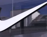 Großes, weißes Nike-Logo auf einer Glasfassade, reflektiert Gebäude im Hintergrund.