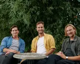 Drei lachende Männer sitzen vor einem Bambus. Sie sind die lfdy inhaber und genießen einen sonnigen Tag.