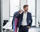 Mann mit Anzügen auf Kleiderbügeln, bereit für die chemische Reinigung.