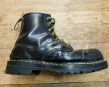 Schwarzer Dr. Martens Stiefel mit gelben Schnürsenkeln und einer neuen, robusten Sohle auf Holzuntergrund.