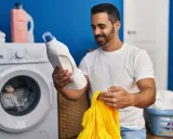 Mann hält Waschmittel und ein gelbes Trikot bereit, um die Wäsche zu waschen.