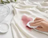 Hand tupft mit weißem Tuch auf rotweinflecken, um sie zu entfernen. Eiswasser und Reiniger liegen bereit.