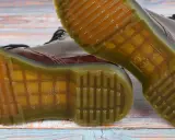 Die charakteristische, gelbe Naht und das Profil der **Dr. Martens Sohle original** sind auf dem Holzuntergrund zu sehen.