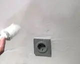 Mit einem Schwamm wird die Wand bearbeitet, um Wasserflecken zu entfernen. Eine Steckdose ist sichtbar.