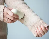 Frauenhand entfernt mit einem Hausmittel Fussel von einem Strickpullover.