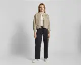 Frau stylt eine beige Bomberjacke mit weiten schwarzen Jeans und weißen Sneakern. Ein lässiger Look, der sich leicht anpassen lässt.