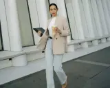 Frau in **smart casual** Kleidung mit Blazer, Jeans und Kaffeebecher geht mit Tablet.