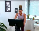 Frau lacht auf einem Heimtrainer, bereit für ein intensives Tabata Workout. Wandbilder motivieren: "Do what you love".