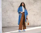 Stilvolles Outfit: Blaue Oversize-Jacke, cremefarbene Bluse mit Schleife und braune weite Hose kombinieren. Accessoires: Korbtasche, Gürtel, Halstuch.