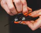 Hände mit orangen Nägeln stellen ein Springseil ein. Die Griffe haben ein Logo.