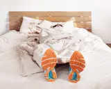 Füße mit Laufschuhen ragen aus einer Decke. Der Wecker klingelt, aber die Person träumt noch vom morgens joggen.