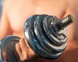 Mann hebt Hantel. Die Frage "wie lange dauert muskelaufbau" beschäftigt viele Fitnessbegeisterte.