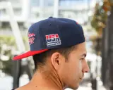 Junger Mann trägt eine dunkelblaue Kappe mit rotem Schirm und "USA Basketball"-Aufdruck, den **cap nach hinten tragen** ist sein Stil.
