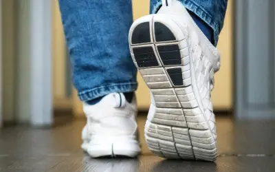 Weiße Turnschuhe mit Jeans. Die Sohle der Schuhe quietschen auf dem Boden, als jemand einen Schritt macht.