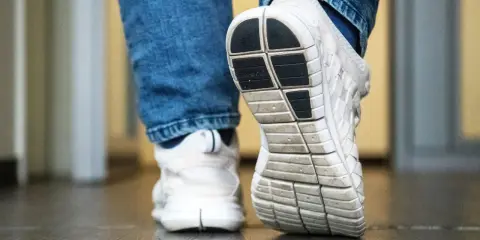 Weiße Turnschuhe mit Jeans. Die Sohle der Schuhe quietschen auf dem Boden, als jemand einen Schritt macht.