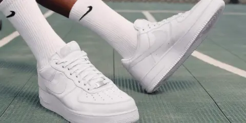 Weiße Nike Air Force 1 Sneaker mit schwarzen Socken auf einem grünen Untergrund. Perfekt zum Air Force 1 binden und loslegen.