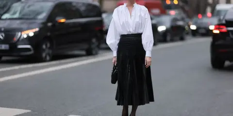 Chic Frau in weißer Bluse und schwarzem oberteil zu plisseerock, steht auf Zebrastreifen.