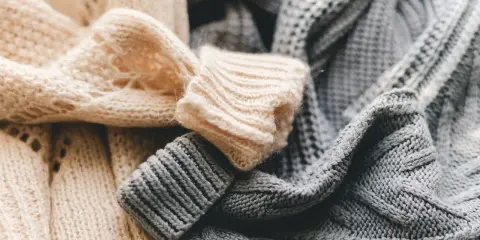 Weiche, gestrickte Pullover in Beige und Grau liegen übereinander. Bald ist Zeit für die **Wolle waschen**, damit sie wieder frisch duften.