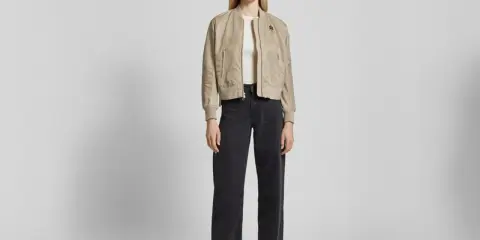 Frau stylt eine beige Bomberjacke mit weiten schwarzen Jeans und weißen Sneakern. Ein lässiger Look, der sich leicht anpassen lässt.