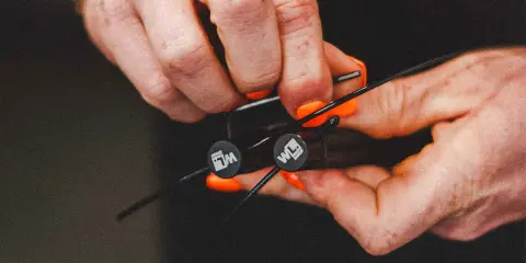 Hände mit orangen Nägeln stellen ein Springseil ein. Die Griffe haben ein Logo.