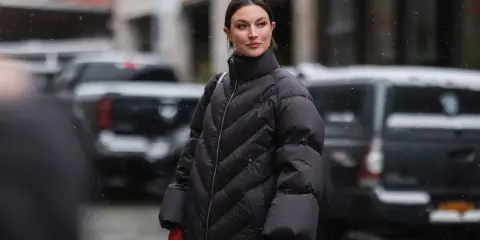 Frau in schwarzer Daunenjacke mit roten Handschuhen im Schnee. Für die Pflege der Daunenjacke im Trockner: welches Programm ist am besten?