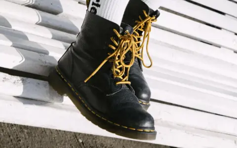 Schwarze Dr. Martens mit gelben Schnürsenkeln auf einer weißen Bank. Sie fallen eher groß aus, also lieber eine Nummer kleiner wählen.