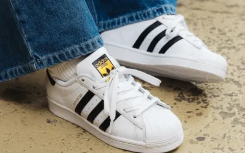 Weiße Adidas Superstar Sneaker mit schwarzen Streifen und gelbem Logo. Perfekt, um das Adidas modell herausfinden.