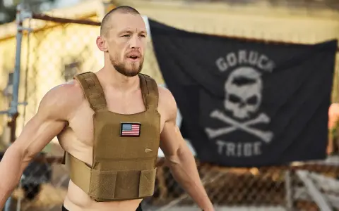 Mann mit Gewichtsweste und GORUCK-Flagge im Hintergrund, bereit für die Murph Challenge.