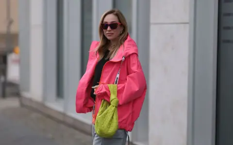 Stylische Frau in knallpinker Jacke und Sonnenbrille. Perfekt, um was anziehen bei 15 Grad. Dazu eine grüne Tasche.
