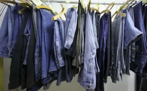 Eine Reihe von Jeans hängt an Kleiderbügeln. Manche sind hellblau, andere dunkelblau. Sie sind bereit, um sie bei 60 Grad zu waschen.