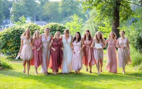 Brautjungfern in zarten Rosatönen, ein perfekter **dresscode hochzeit**, spazieren lachend über eine grüne Wiese.