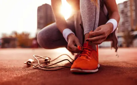 Sportlerin bindet ihre neuen, leuchtend orangen Laufschuhe ein. Die Sonne scheint, ein Springseil liegt bereit.