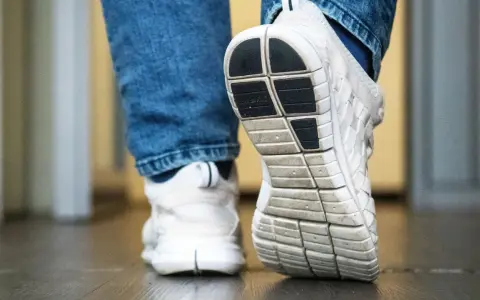 Weiße Turnschuhe mit Jeans. Die Sohle der Schuhe quietschen auf dem Boden, als jemand einen Schritt macht.