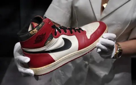 Ein Paar rote und weiße Air Jordan 1 Sneaker, die als die teuersten Schuhe der Welt gelten, werden von Händen in weißen Handschuhen gehalten.