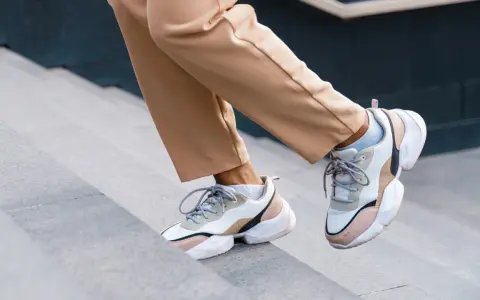 Schritte aufwärts in beigen Hosen und trendigen Sneakern mit sichtbaren Socken. Der socken in sneaker trend ist hier perfekt umgesetzt.