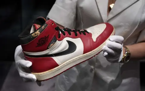 Ein ikonischer Air Jordan 1 Sneaker, der die Nike Air Jordan Geschichte verkörpert, wird von Händen in weißen Handschuhen präsentiert.