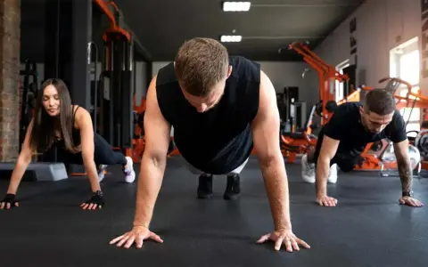 Drei Personen machen Liegestütze im Fitnessstudio. Sie lernen, was sind Burpees, eine Ganzkörperübung.