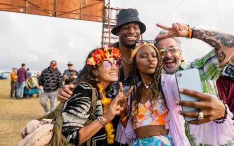 Bunte Outfits, Blumenkränze und Peace-Zeichen: So zieht man zu einem Rave an! Vier Freunde machen ein Selfie.