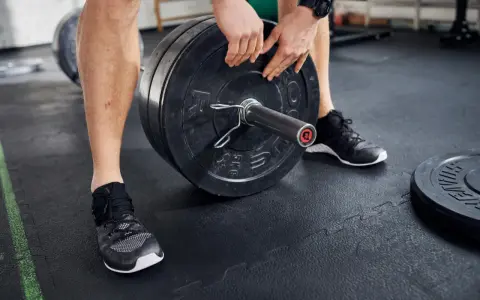 Mann lädt Gewichtsscheiben auf eine Langhantel in einem Fitnessstudio.