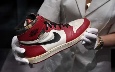 Ein Paar abgenutzte Air Jordan 1 Sneaker, die seit 1985 erhältlich sind, werden von einer Person mit weißen Handschuhen gehalten.