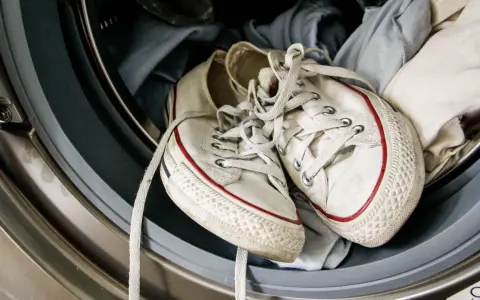 Weiße Turnschuhe mit roten Streifen liegen in einer Waschmaschine, bereit für die Reinigung.