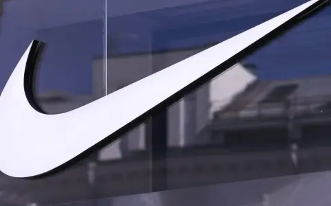 Großes, weißes Nike-Logo auf einer Glasfassade, reflektiert Gebäude im Hintergrund.