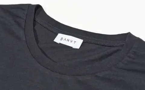 Dunkelgraues T-Shirt mit weißem Etikett "SANVT". Perfekt für den Sommer, ab 20 Grad tragbar.