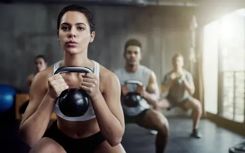 Frau führt Kettlebell-Squats aus, Teil einer intensiven Metcon-Trainingseinheit mit anderen Trainierenden im Hintergrund.