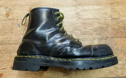 Schwarzer Dr. Martens Stiefel mit gelben Schnürsenkeln und einer neuen, robusten Sohle auf Holzuntergrund.