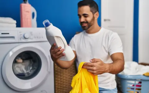 Mann hält Waschmittel und ein gelbes Trikot bereit, um die Wäsche zu waschen.