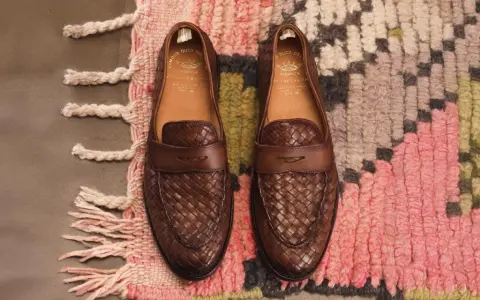 Zwei braune Leder-Loafer mit geflochtenem Muster, Marke Officine Creative, liegen auf einem bunten Teppich.