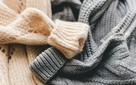 Weiche, gestrickte Pullover in Beige und Grau liegen übereinander. Bald ist Zeit für die **Wolle waschen**, damit sie wieder frisch duften.