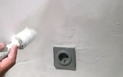 Mit einem Schwamm wird die Wand bearbeitet, um Wasserflecken zu entfernen. Eine Steckdose ist sichtbar.
